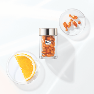 Stylized image of MULTI CORREXION® Revive + Glow Vitamin C Night Serum Capsules bottle and capsules next to an orange slice