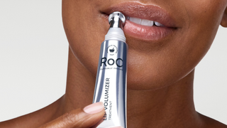 Person using a RoC lip volumizer on their lips with a plain background