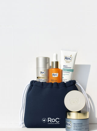 RoC skincare products (Revive + Glow Daily Serum, Hydration+ Moisturizer SPF, Derm Correxion Firming Serum Stick, Derm Correxion Dual Eye Cream, Firm + Lift Anti-Sagging Cream) with a navy holiday cosmetic bag on a white background