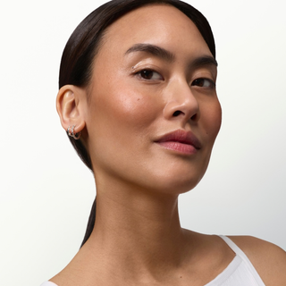 A close-up portrait of a woman with her hair pulled back, wearing a small silver hoop earring with a clear gemstone, against a clean white background.