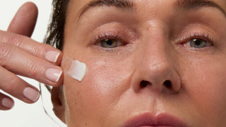 Close-up of a person applying cream to their face with a neutral background
