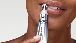 Person using a ROC lip volumizer on their lips with a plain background