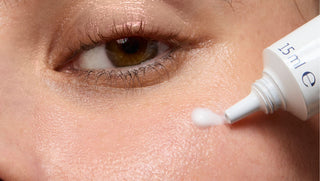 Close-up of a person applying a white cream to their under eye with a dropper bottle.