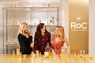 Three women laughing together in a room with shelves and a table displaying RoC products.