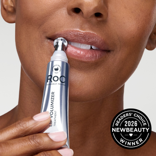 Close-up of a woman holding a silver and white ROC Lip Volumizer treatment tube near her lips, with a black 'Readers' Choice 2026 NewBeauty Winner' badge in the lower right corner.