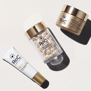 Three ROC skincare products arranged diagonally on a light beige background with dramatic shadows: a white tube of Retinol Cream, a clear jar of Retinol Correction soft gel capsules, and a gold-lidded cream jar of Retinol Correction Vial Moisturizing Face Cream.