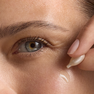 Close-up of a woman applying a line smoothing night serum capsule to her face.