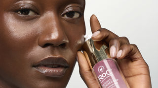 Close-up of a person holding a bottle of ROC Retinol Correxis Retinol 1% + 0.05% Hexylene Glycol 1ml pump against a light gray background.
