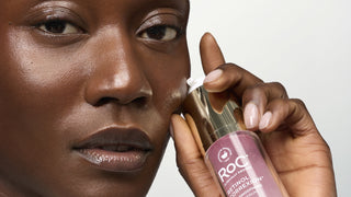 Close-up of a person holding a bottle of ROC Retinol Correxis Retinol 1% + 0.05% Hexylene Glycol 1ml pump against a light gray background.